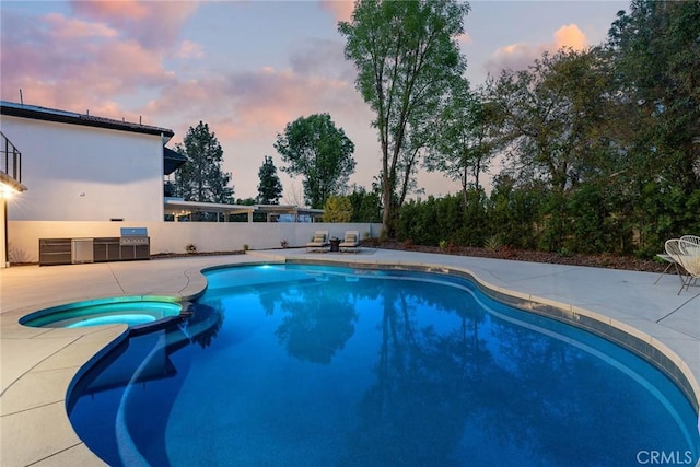 pool at dusk featuring fence, a pool with connected hot tub, and a patio area