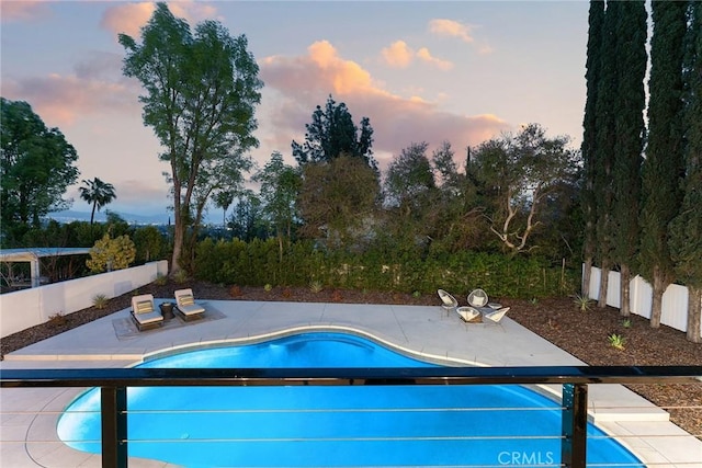 pool at dusk featuring fence, a fenced in pool, and a patio