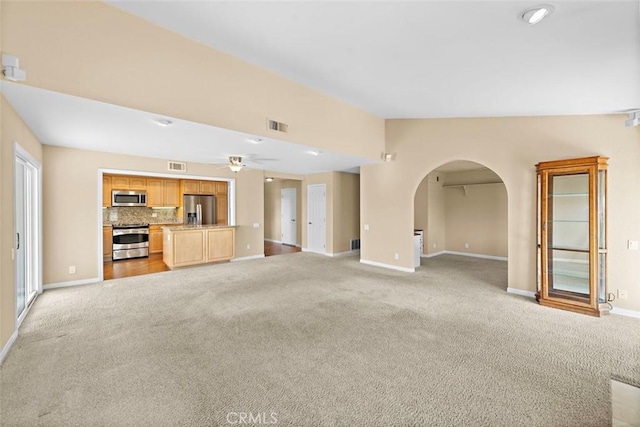 unfurnished living room featuring light carpet, visible vents, arched walkways, and lofted ceiling