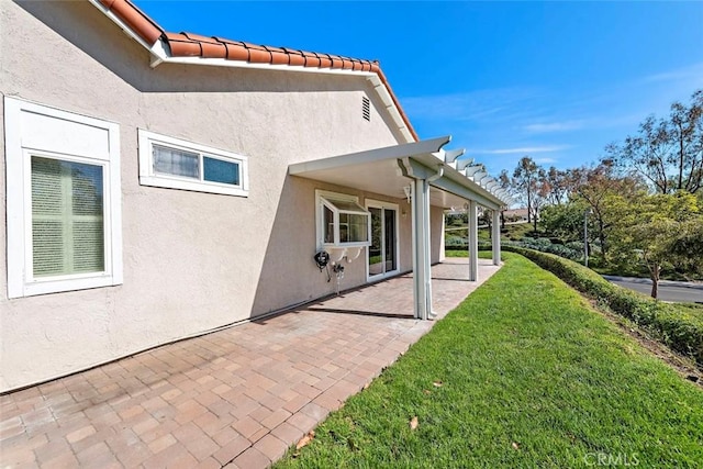 exterior space featuring a yard, a patio, a tiled roof, and stucco siding