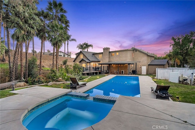 pool at dusk with a pool with connected hot tub, a fenced backyard, and a patio