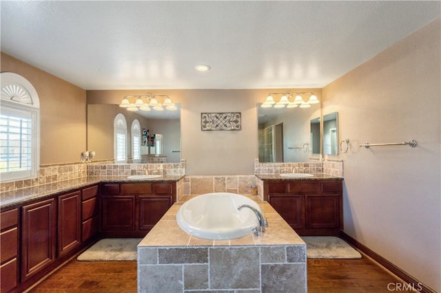 full bath with a bath, two vanities, a sink, and wood finished floors