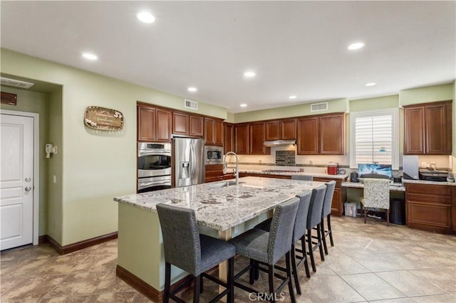 kitchen featuring a breakfast bar area, visible vents, appliances with stainless steel finishes, an island with sink, and under cabinet range hood