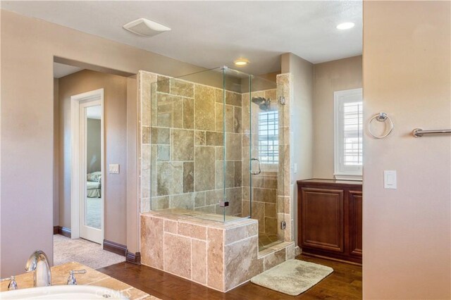 full bathroom featuring a sink, a shower stall, wood finished floors, baseboards, and a bath