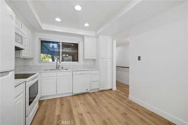 kitchen with a sink, white appliances, light wood finished floors, light countertops, and white cabinetry