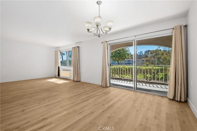 spare room featuring light wood-style floors, baseboards, and a notable chandelier