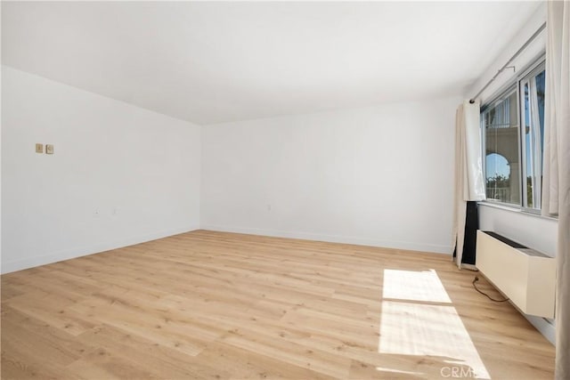 spare room with light wood-style flooring, baseboards, and radiator