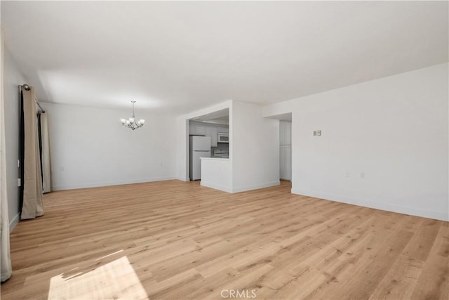 unfurnished living room featuring baseboards, a notable chandelier, and light wood-style flooring