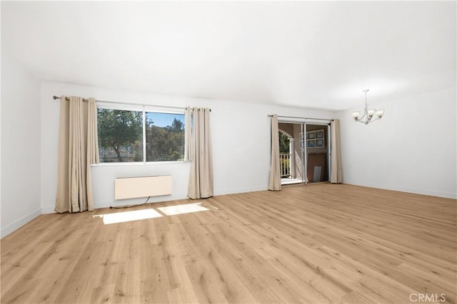 unfurnished room featuring light wood finished floors, baseboards, a notable chandelier, and radiator