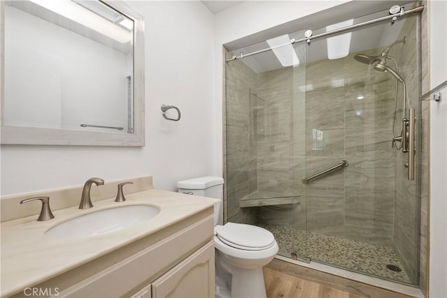 bathroom with a shower stall, toilet, vanity, and wood finished floors