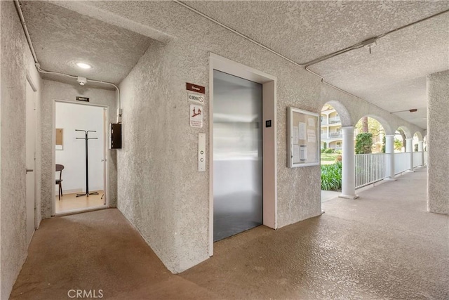 corridor with elevator and a textured ceiling