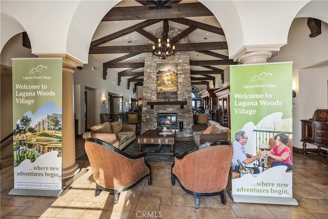 living room featuring a stone fireplace, a chandelier, vaulted ceiling with beams, arched walkways, and decorative columns