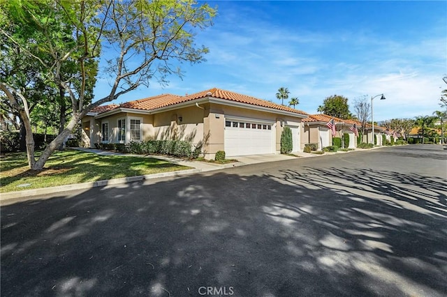 mediterranean / spanish home featuring a garage, driveway, stucco siding, a tile roof, and a front yard