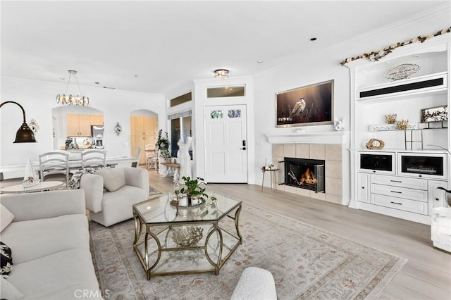 living room with ornamental molding, arched walkways, a tiled fireplace, and wood finished floors