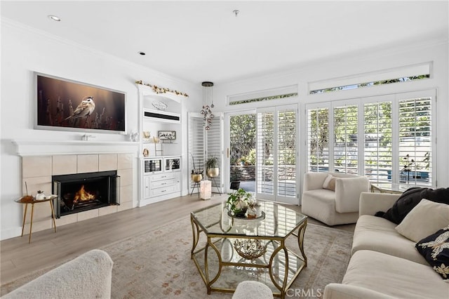 living area with ornamental molding, built in shelves, a tiled fireplace, and plenty of natural light