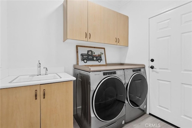 clothes washing area with light wood-style floors, washing machine and dryer, cabinet space, and a sink