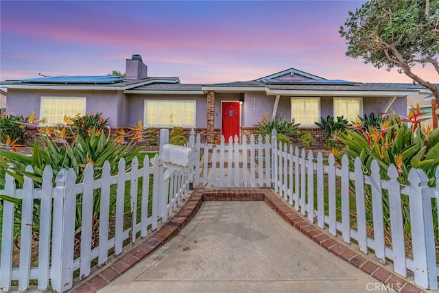 ranch-style home featuring stucco siding, a fenced front yard, a chimney, roof mounted solar panels, and brick siding