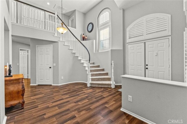 entryway with dark wood finished floors, stairs, baseboards, and a towering ceiling