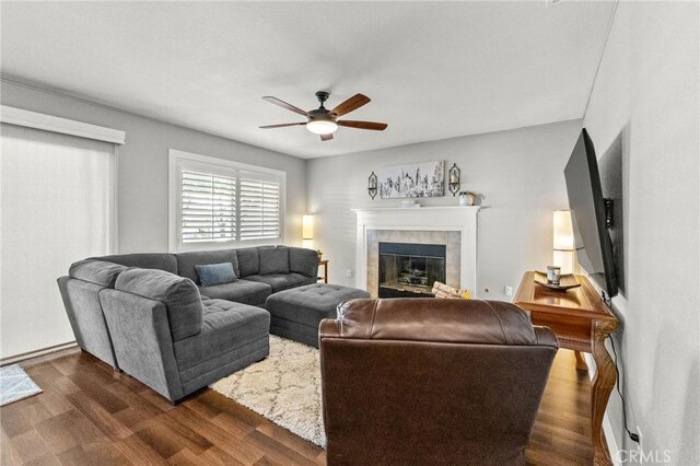 living area featuring a fireplace, dark wood-type flooring, and a ceiling fan