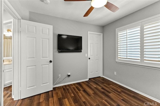 unfurnished bedroom featuring connected bathroom, ceiling fan, baseboards, and dark wood-style flooring