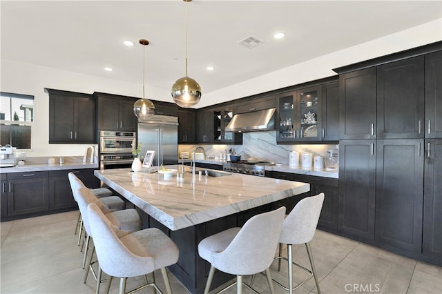 kitchen with under cabinet range hood, stainless steel appliances, a breakfast bar, a sink, and visible vents