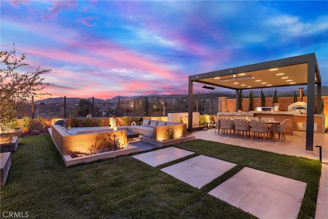 yard at dusk with a patio area, a fenced backyard, a mountain view, and an outdoor kitchen