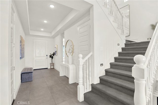 entryway with stairs, a tray ceiling, tile patterned floors, and recessed lighting