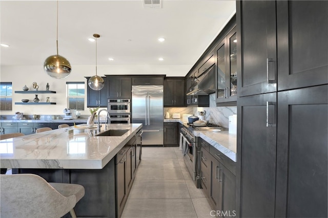 kitchen with tasteful backsplash, high quality appliances, light stone counters, under cabinet range hood, and a sink