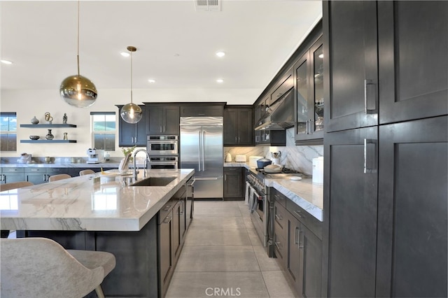 kitchen with under cabinet range hood, premium appliances, light stone countertops, and decorative backsplash