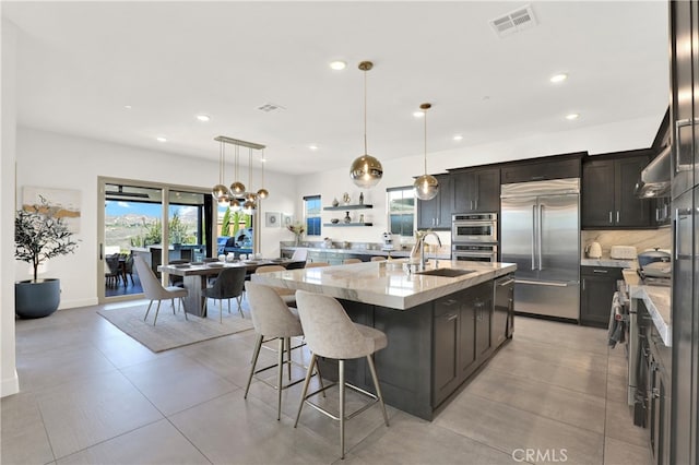 kitchen with tasteful backsplash, appliances with stainless steel finishes, light stone counters, a kitchen bar, and a sink