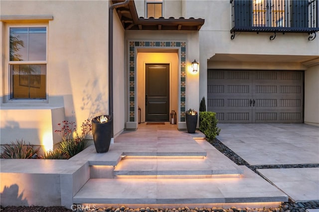 view of exterior entry featuring a garage, concrete driveway, and stucco siding