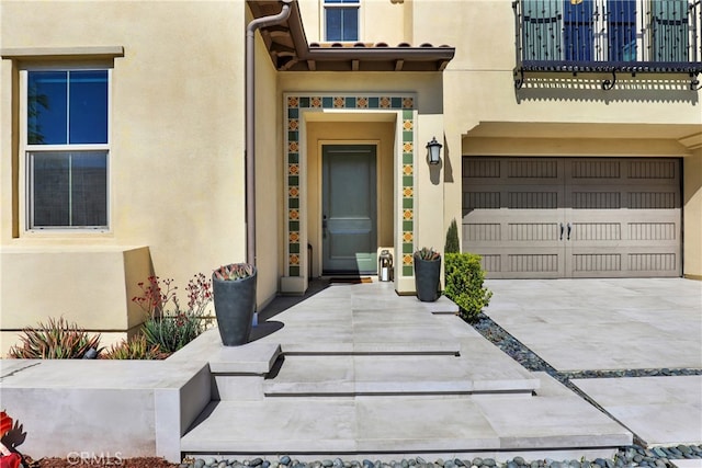 entrance to property with a garage, concrete driveway, and stucco siding