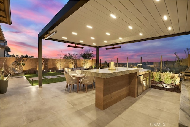 patio terrace at dusk with outdoor dry bar, exterior kitchen, and a fenced backyard