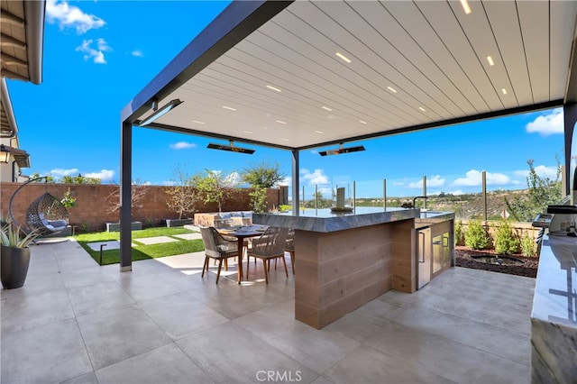 view of patio featuring outdoor wet bar, fence, and an outdoor kitchen