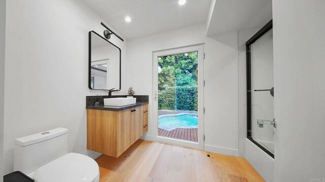 bathroom featuring recessed lighting, toilet, combined bath / shower with glass door, vanity, and wood finished floors