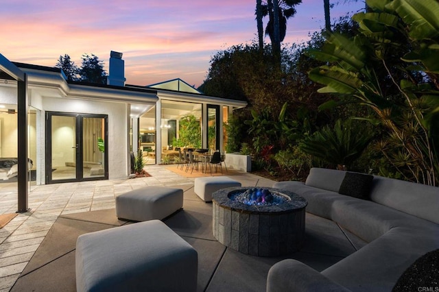 patio terrace at dusk with french doors and an outdoor living space with a fire pit