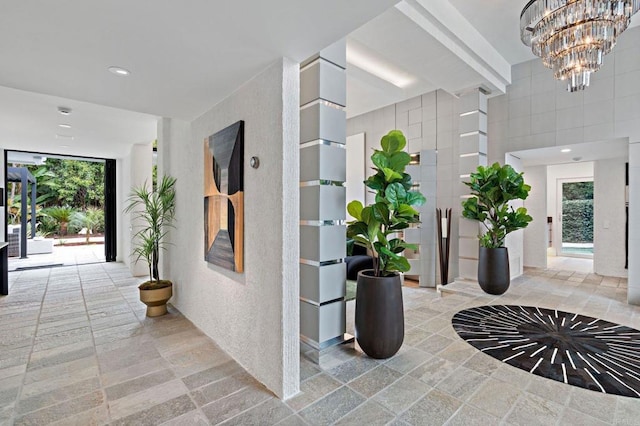 hall with recessed lighting, stone tile flooring, and a notable chandelier