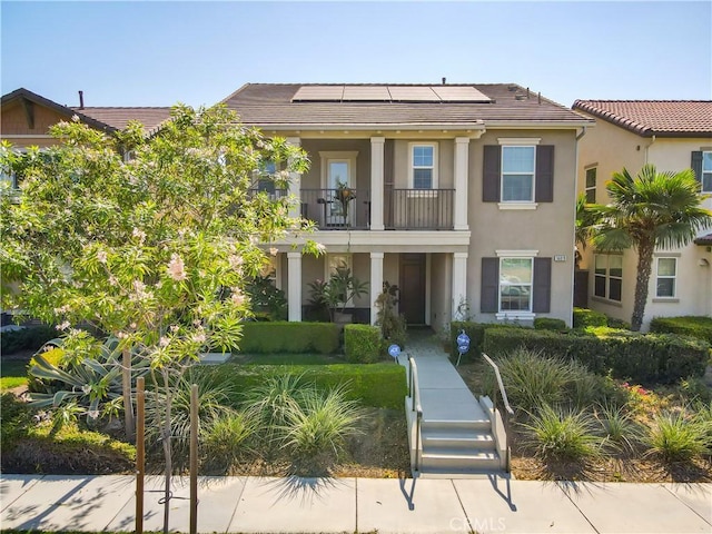 view of front of home featuring a balcony, a tiled roof, solar panels, and stucco siding