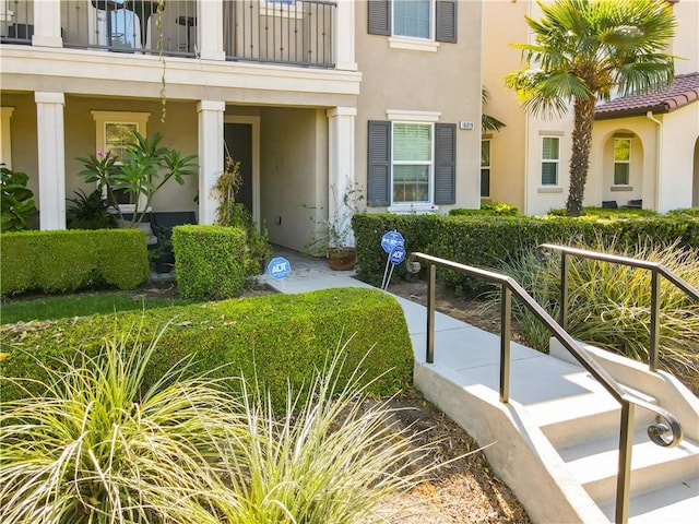 property entrance with covered porch, a balcony, and stucco siding