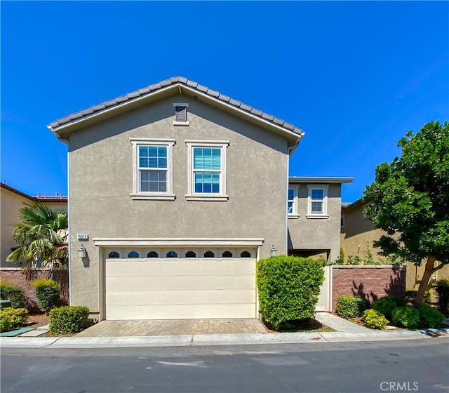 traditional home featuring a tiled roof, decorative driveway, an attached garage, and stucco siding