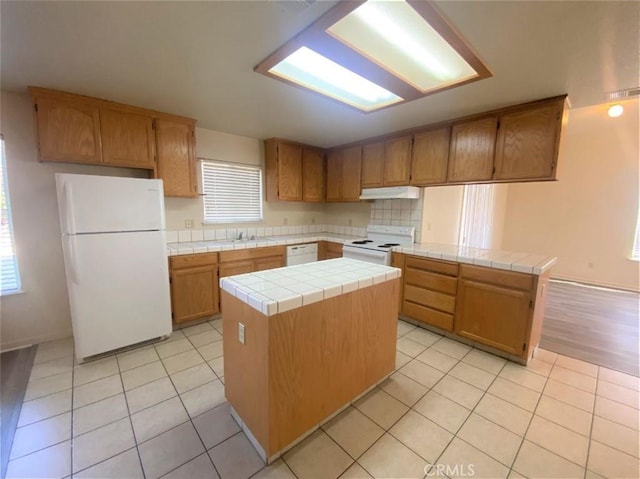 kitchen featuring tile countertops, light tile patterned flooring, under cabinet range hood, white appliances, and a center island