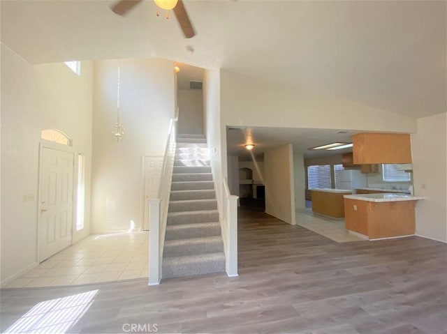 interior space with visible vents, ceiling fan, stairs, light wood-style floors, and high vaulted ceiling