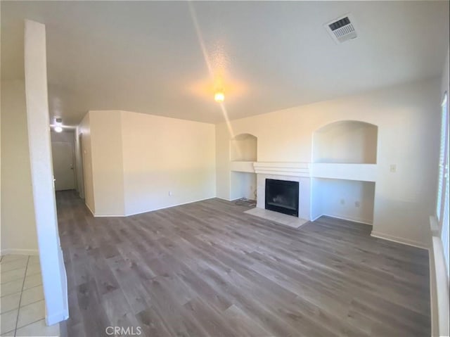 unfurnished living room with baseboards, a fireplace with flush hearth, visible vents, and wood finished floors