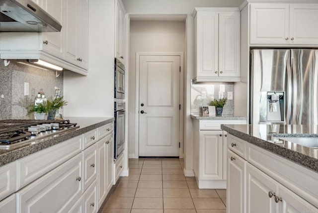 kitchen with light tile patterned floors, under cabinet range hood, white cabinetry, appliances with stainless steel finishes, and decorative backsplash