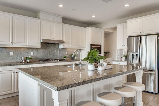 kitchen featuring stainless steel appliances, light tile patterned flooring, a sink, and under cabinet range hood