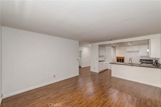 unfurnished living room featuring a sink, baseboards, and dark wood finished floors