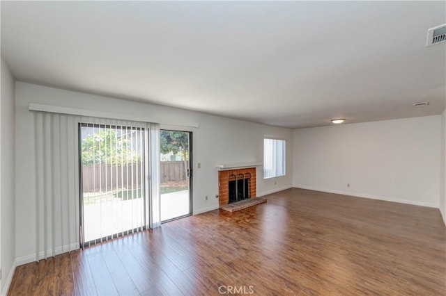 unfurnished living room with a brick fireplace, baseboards, and wood finished floors