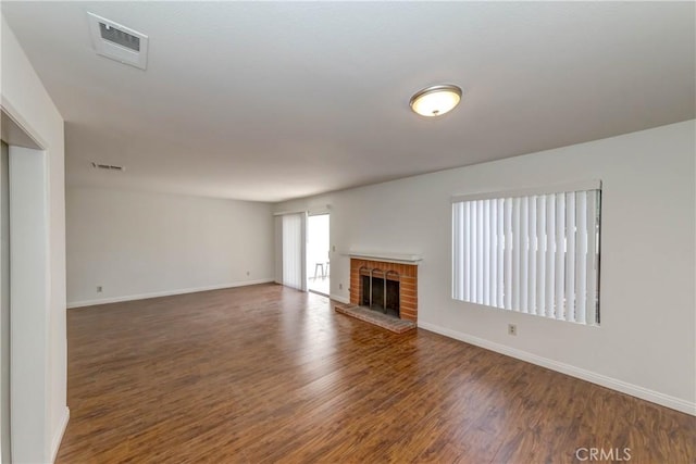 unfurnished living room featuring a brick fireplace, wood finished floors, visible vents, and baseboards