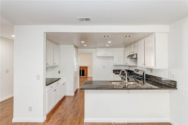 kitchen with dark stone countertops, a sink, white cabinetry, a peninsula, and light wood finished floors