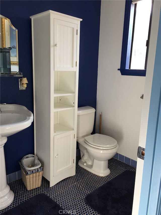 half bathroom with baseboards, toilet, and tile patterned floors